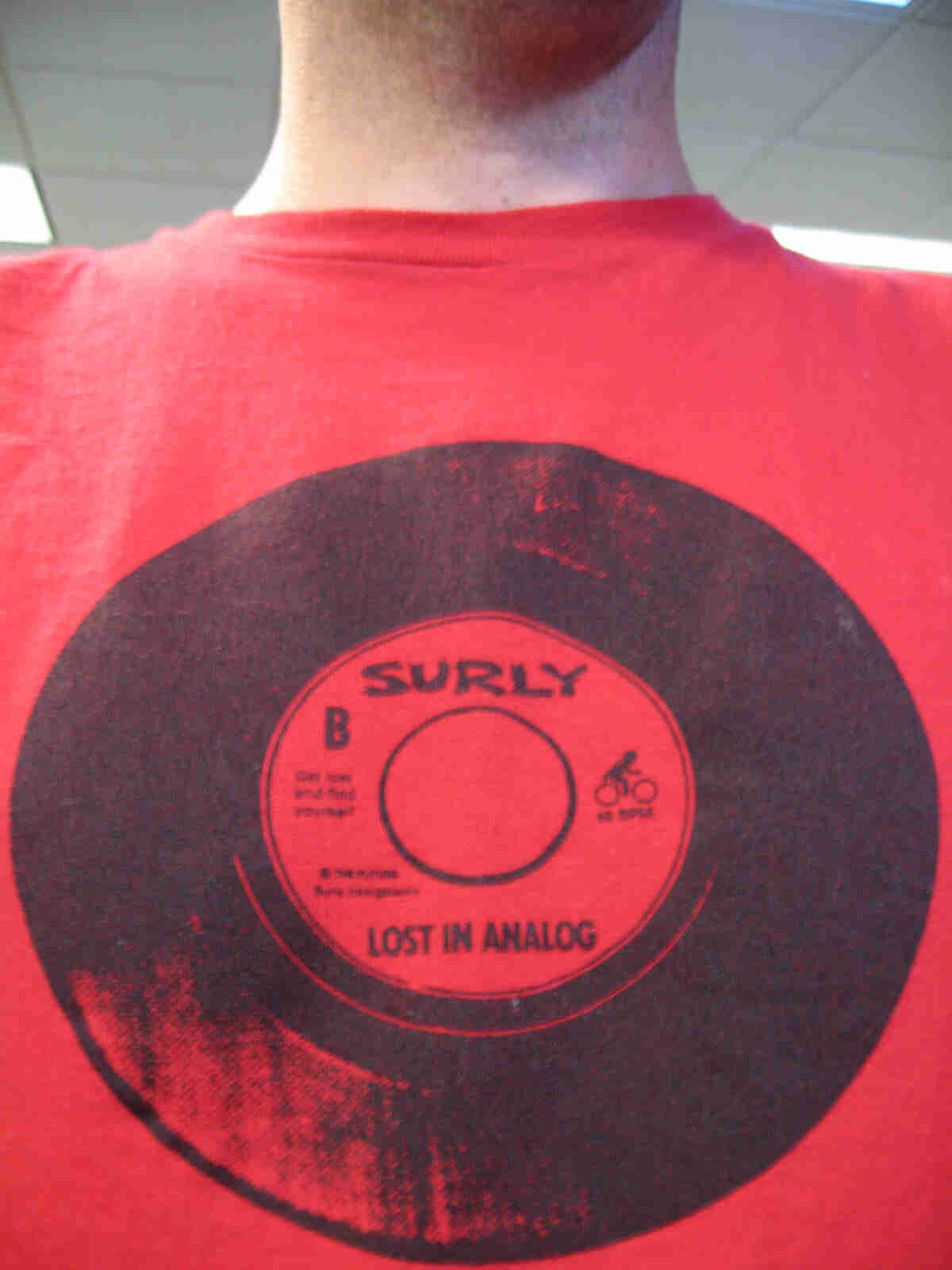 Front, chest area view of a person wearing a red Surly bike t-shirt with a black record album graphic, in an office